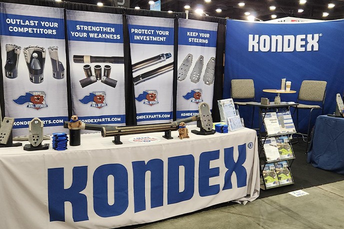 The Kondex booth at a trade show. Products are displayed on a table and banners are in the background