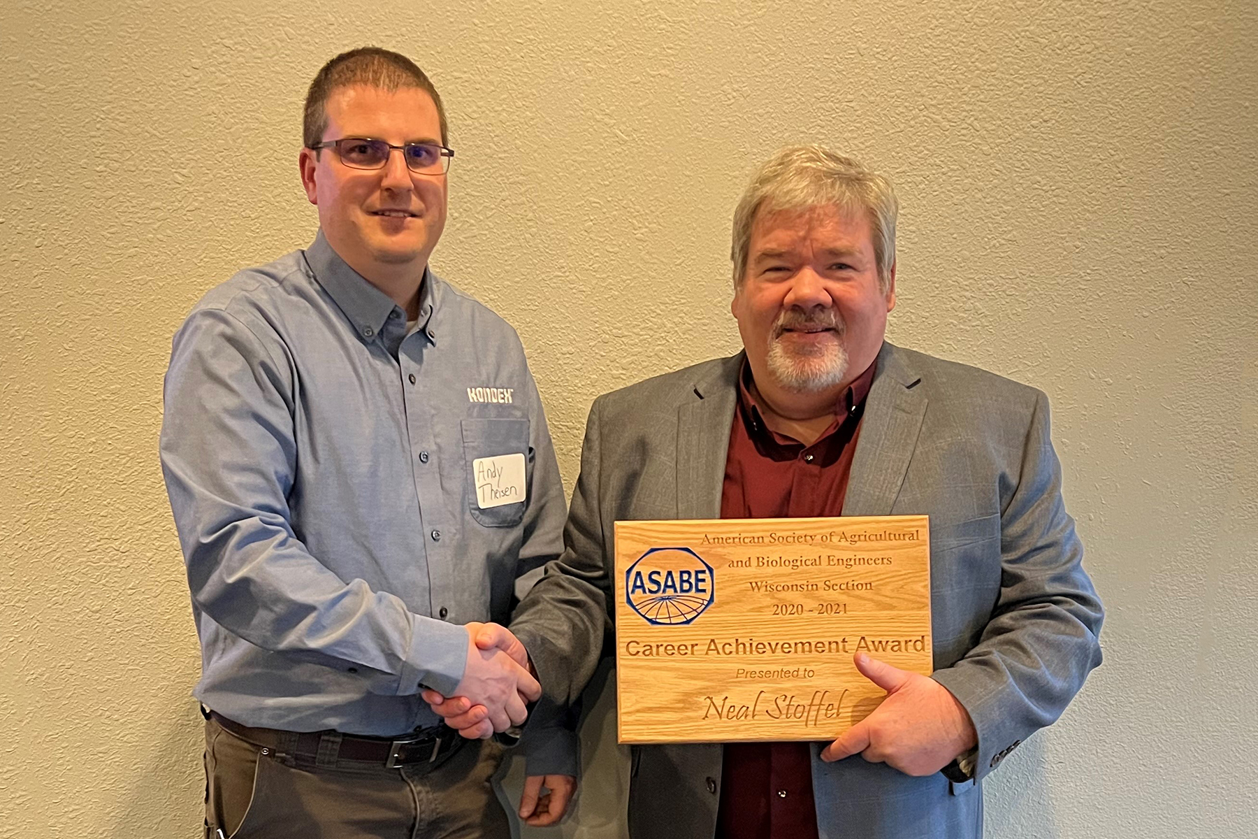 Andy Theisen (left) shakes hands with Neal Stoffel (right) holding award plaque