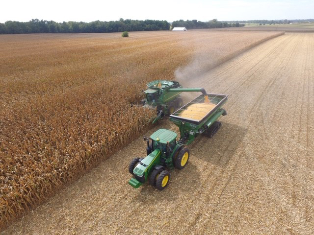 John Deere combine harvesting a large field of corn with grain cart collecting kernels